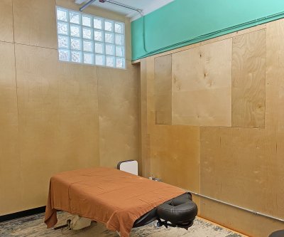 Image of the new Acupuncture Studio at Castle Hill Fitness. It has wooden walls with teal wall trim on top, and a window. There is an Acupuncture treatment bed in the middle of the room, with orange sheets. 