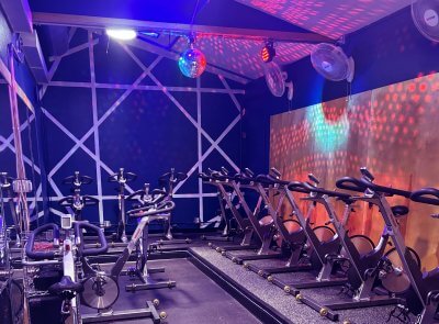 Image of the new Cycle Room at Castle Hill Fitness. It features a row of bikes against a wood wall, in a navy blue room. The back wall has a white geometric lines pattern painted on it. 