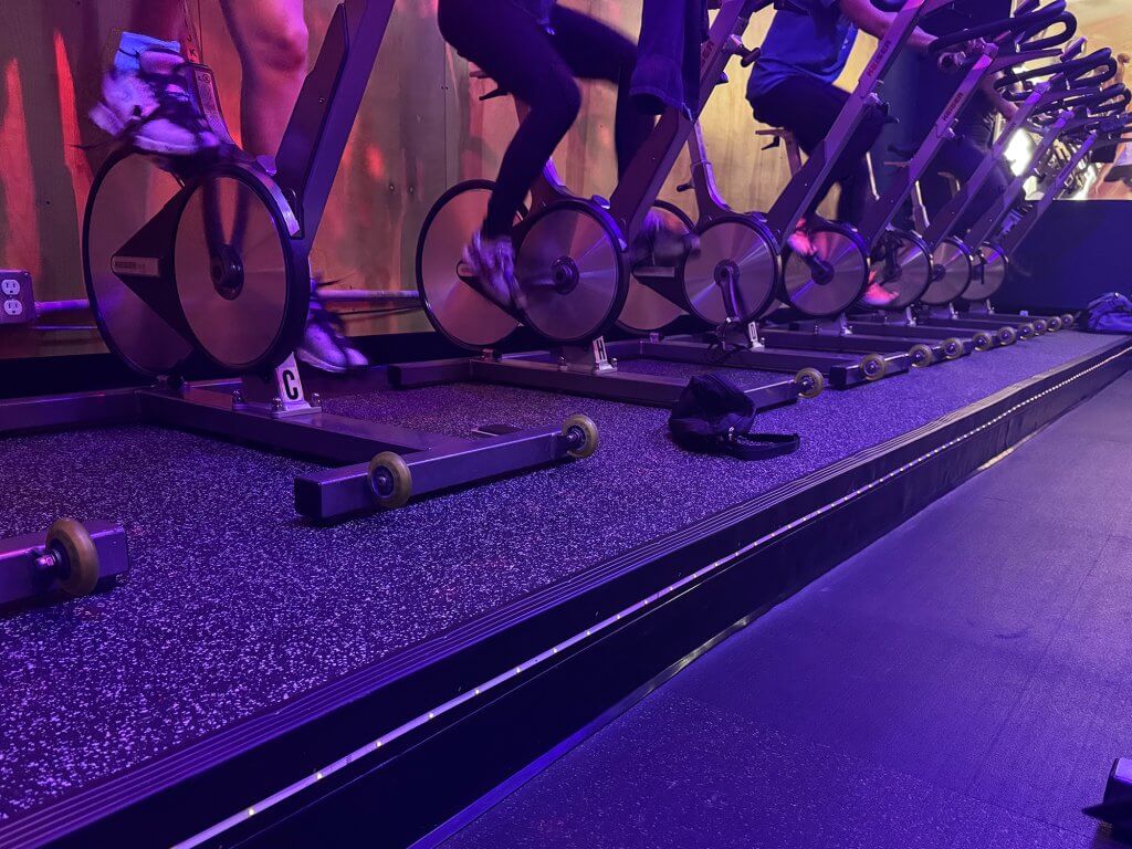 Image of a row of feet spinning on bikes in the new Castle Hill Fitness Cycle Room. The room is colorfully lit.